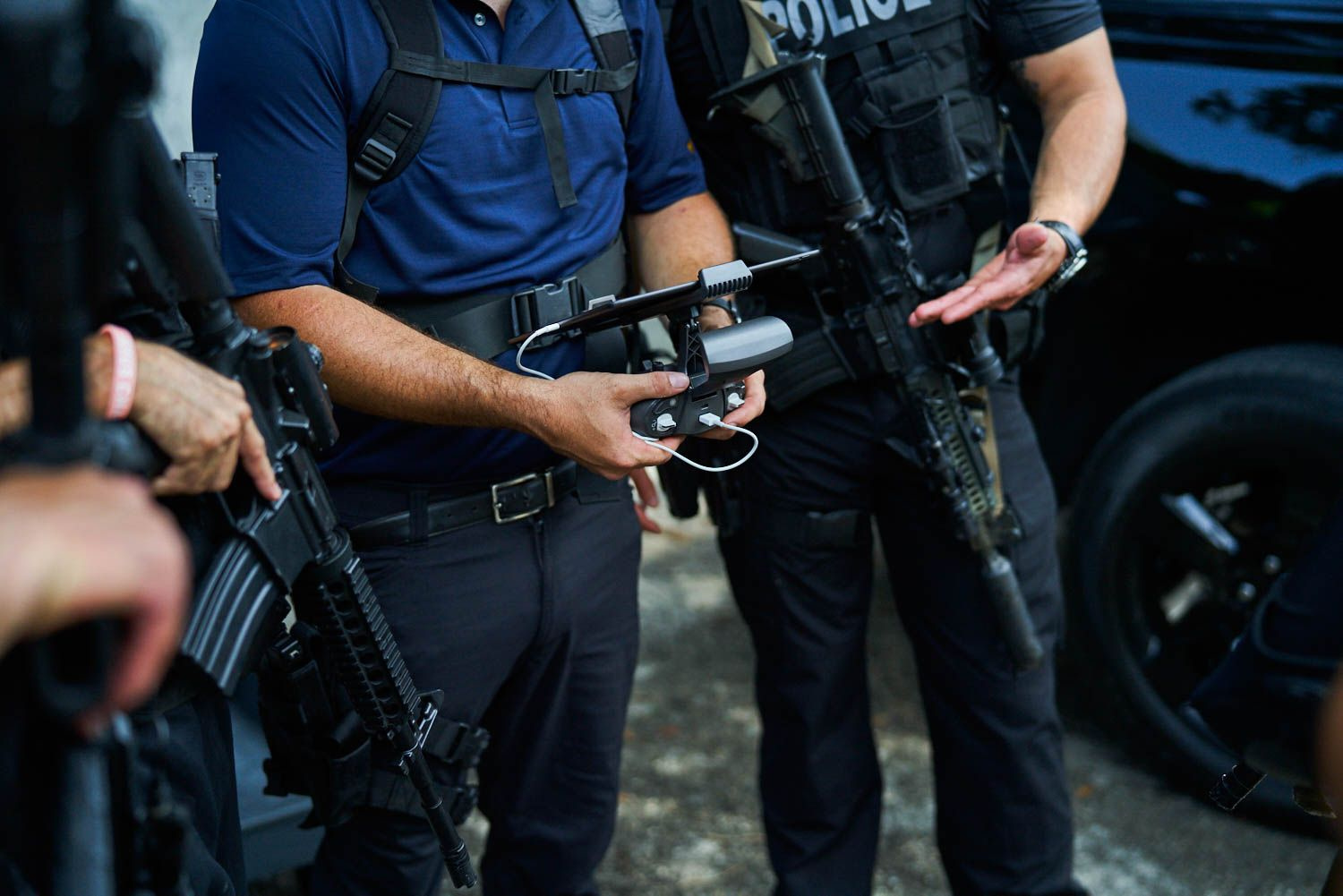 The midriff of 3 people with assault rifles talking to a drone operator with the remote controller as the central focus